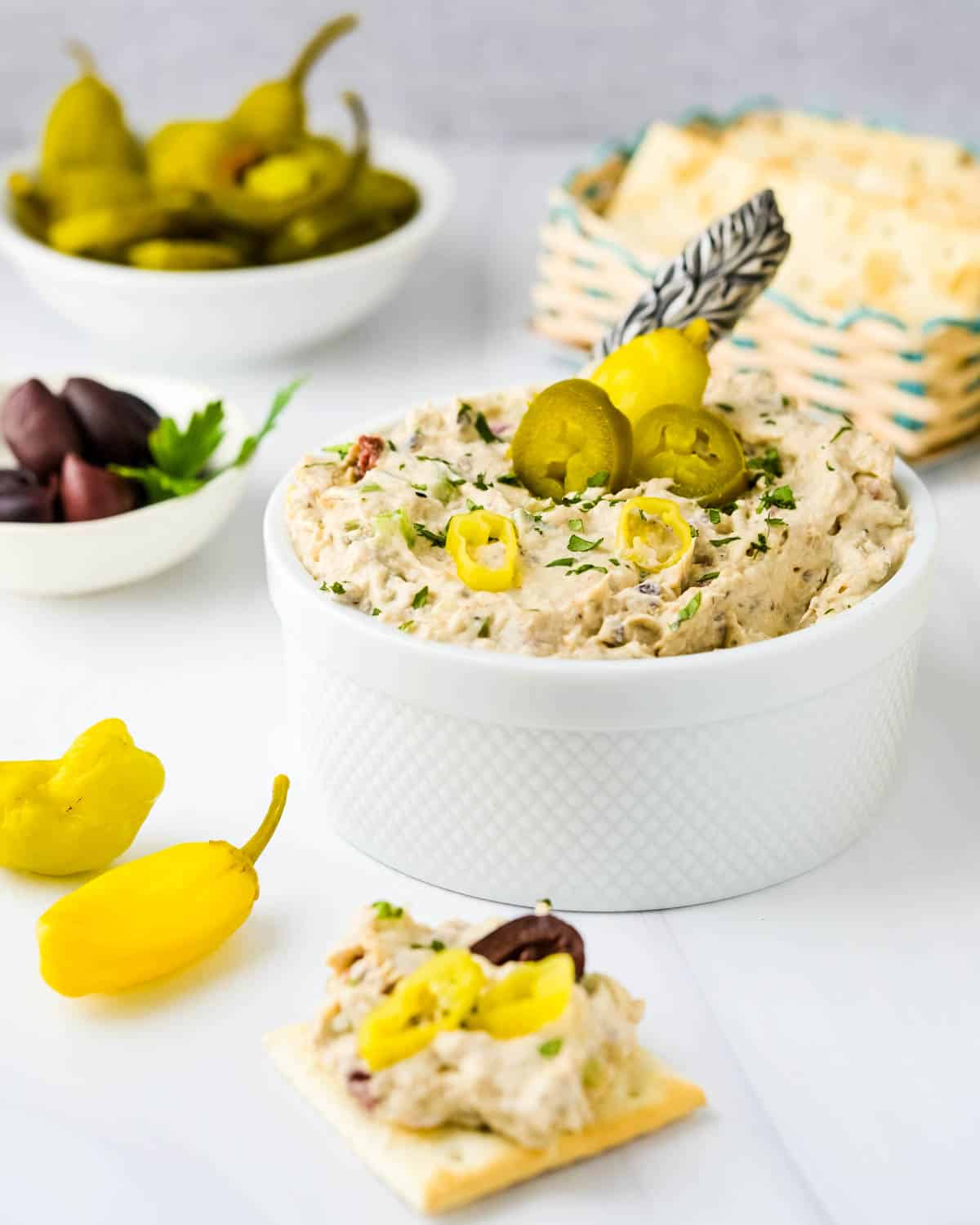 a dish of smoked fish dip with pepperoncini, olives and pickled peppers.