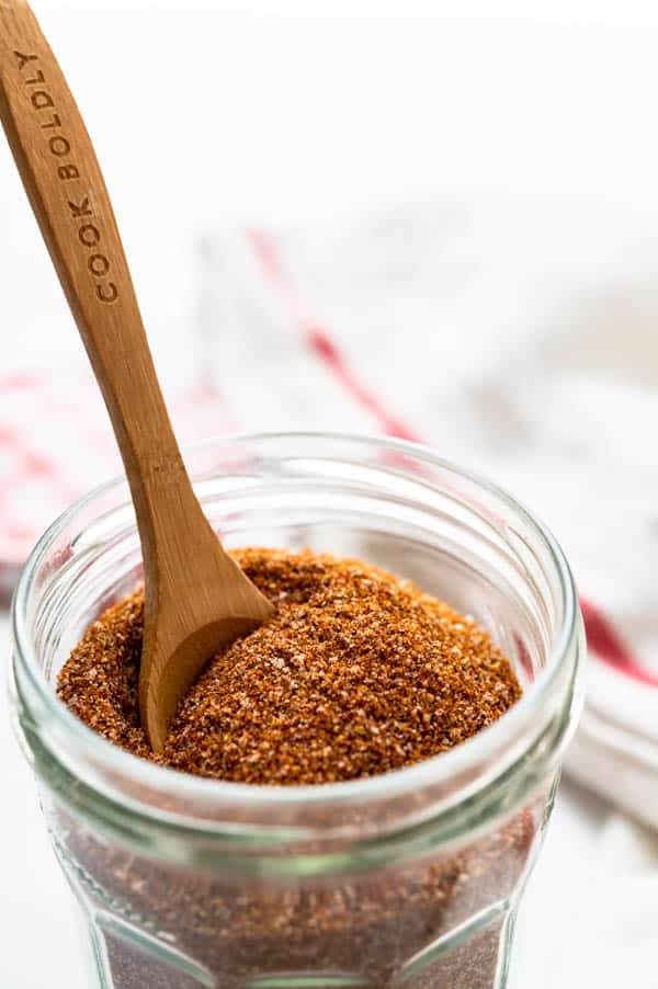 The blended chipotle rub seasoning, in a glass jar with a wooden spoon.