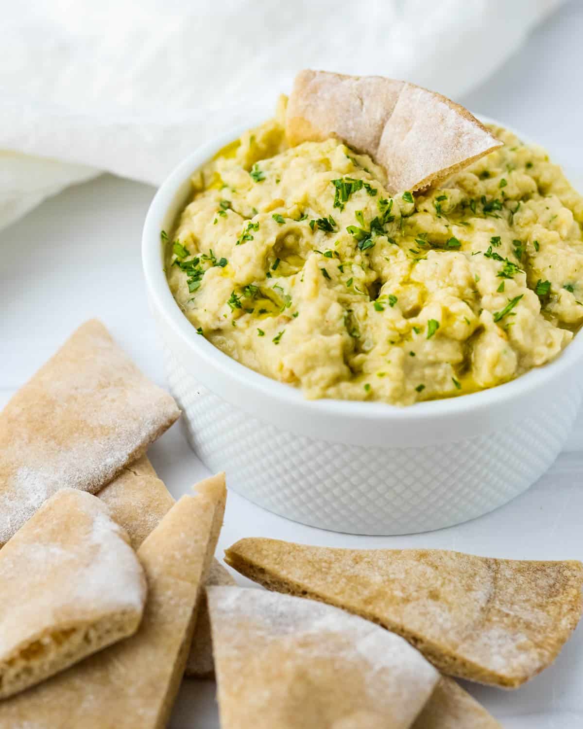 A bowl of baba ganoush surrounded by pita chips.