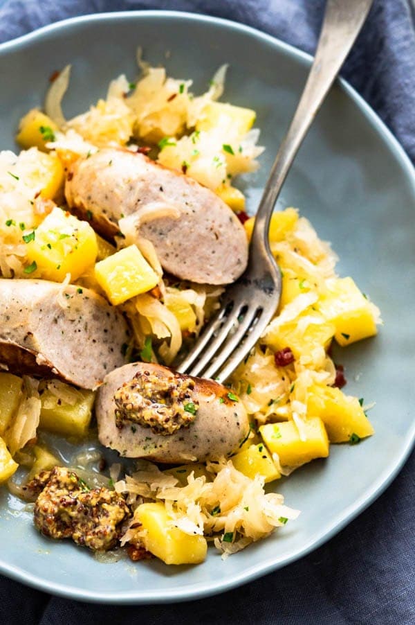 A plate of sausages, sauerkraut and potatoes with whole grain mustard.