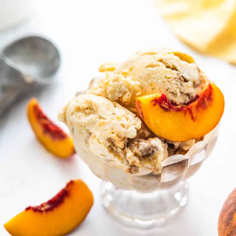 Serving a dish of homemade peach ice cream with streusel topping and fresh peaches.