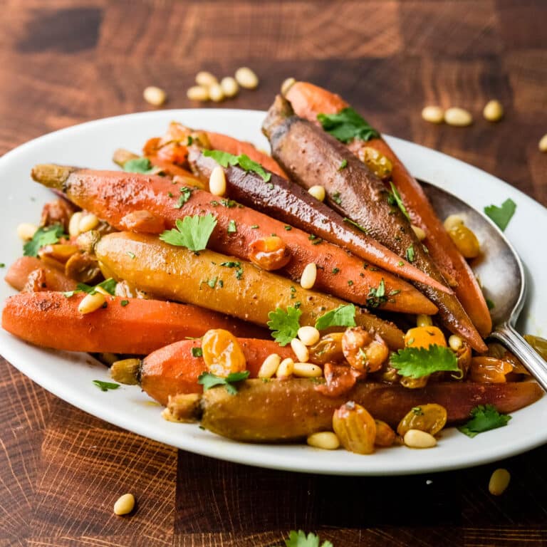 a plate of spiced carrots with raisins and pine nuts.