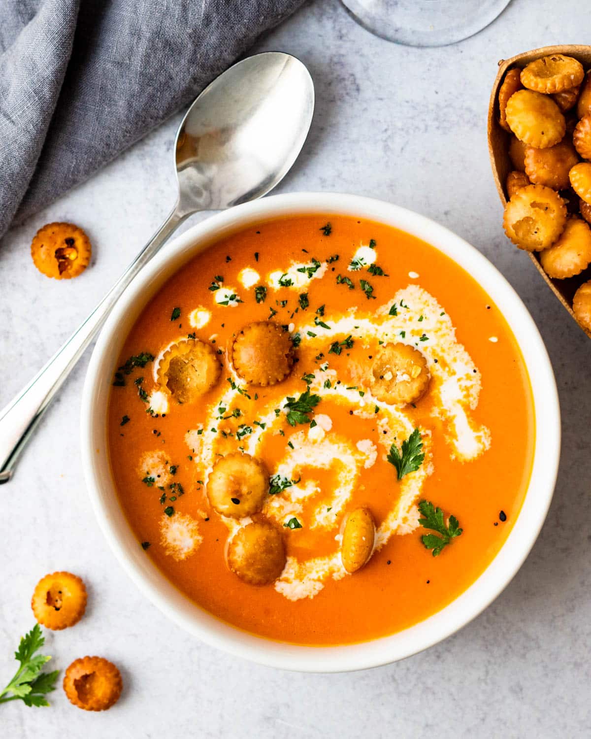A bowl of creamy tomato and bell pepper soup with oyster crackers.