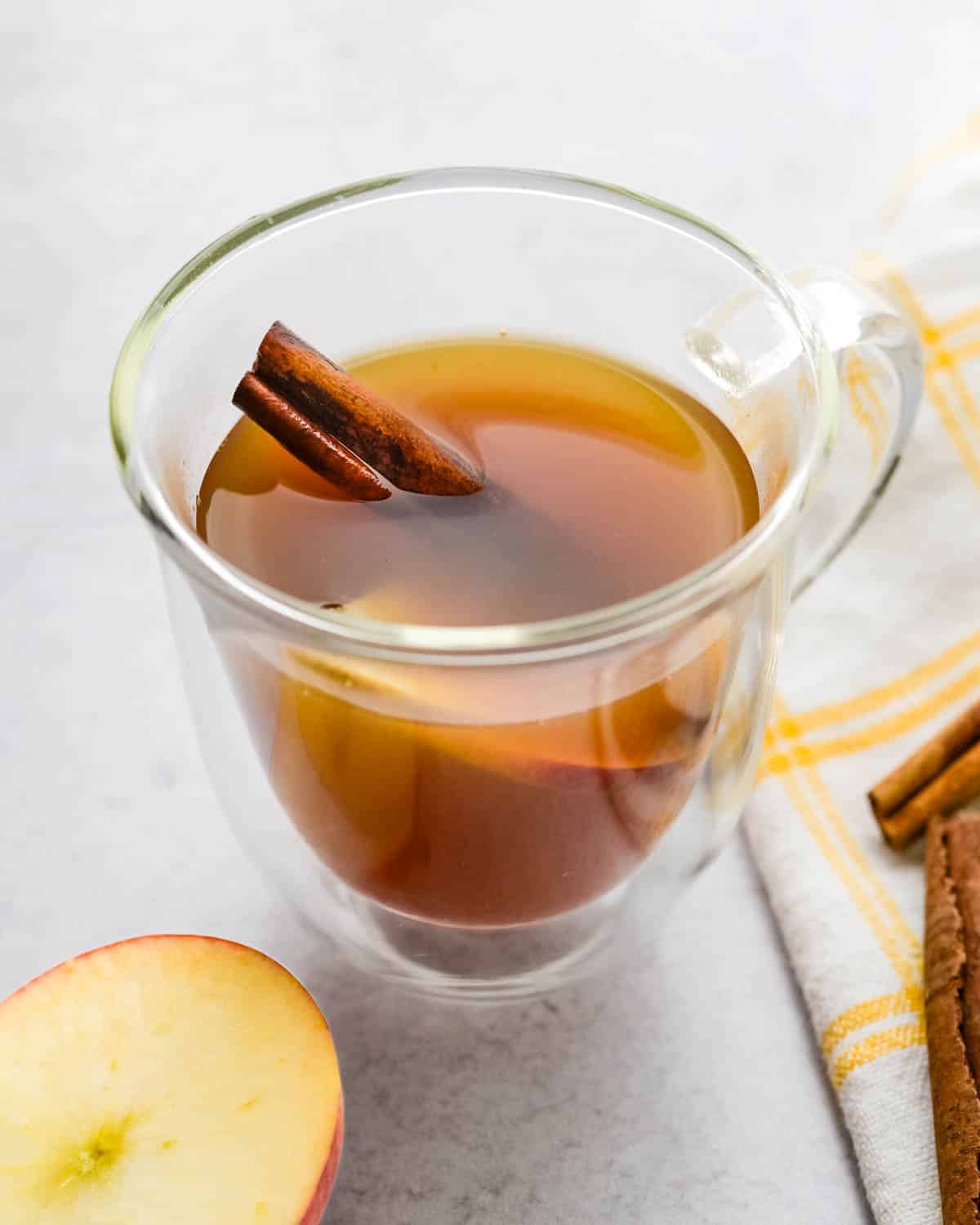 A cup of spiked apple cider tea with a cinnamon stick and a slice of apple.