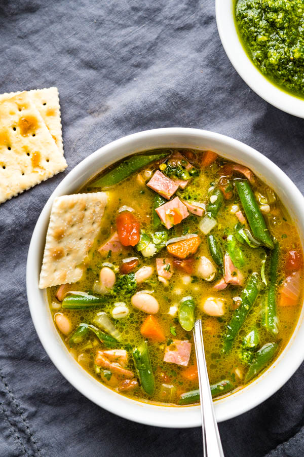 Ham vegetable barley pistou soup in a bowl with saltine crackers.