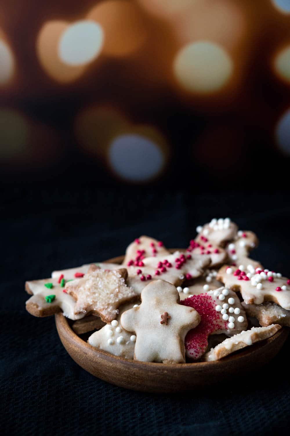 A plate of decorated Christmas cookies with a background of twinkling lights.