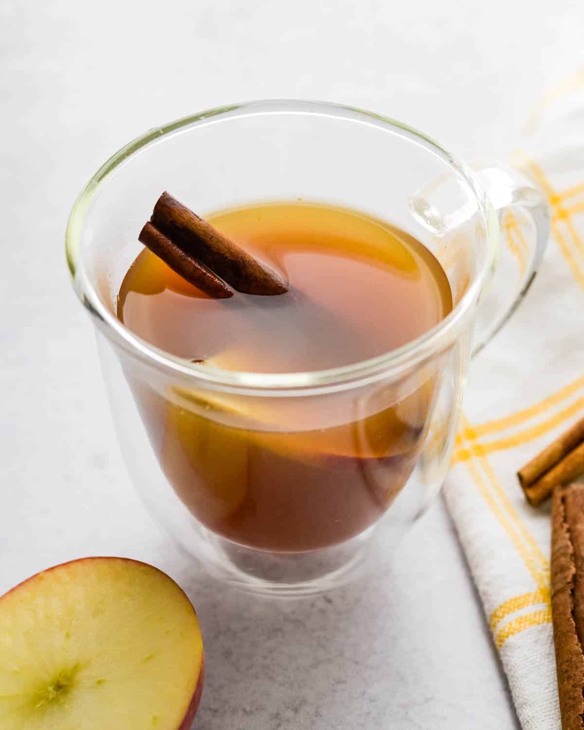 a steaming cup of the hot apple cider tea with a cinnamon stick.