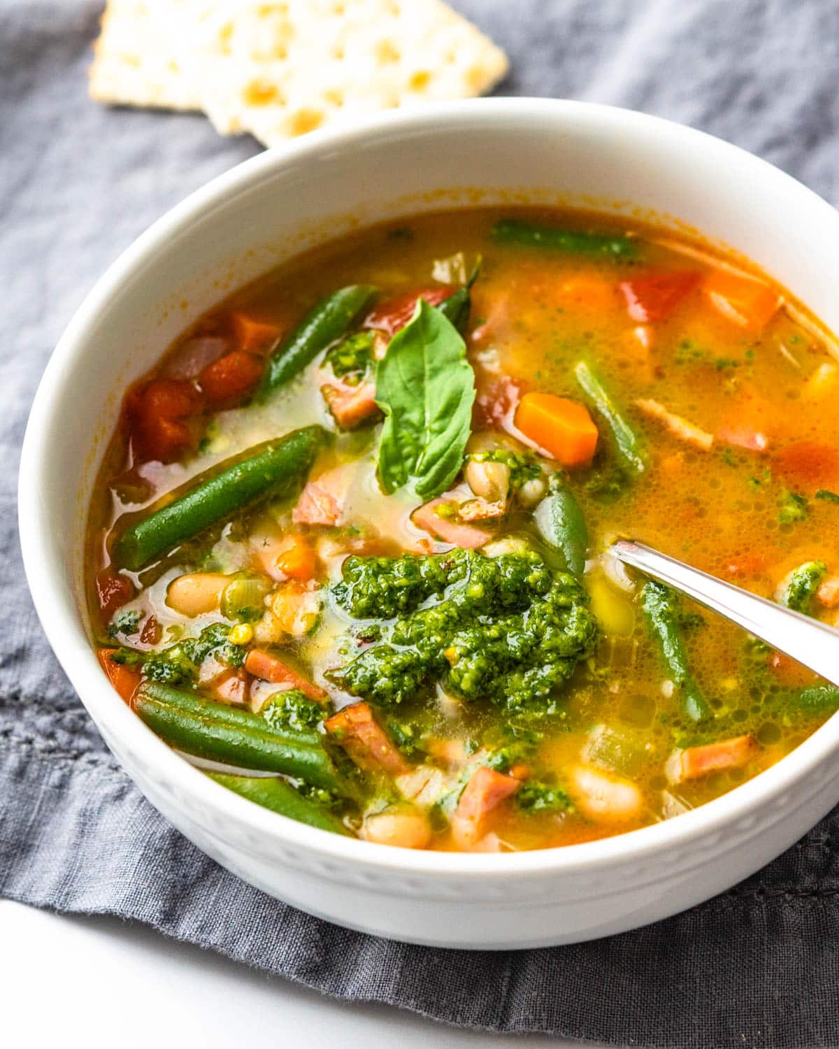 a bowl of ham and vegetable soup with a scoop of fresh bsil pistou.