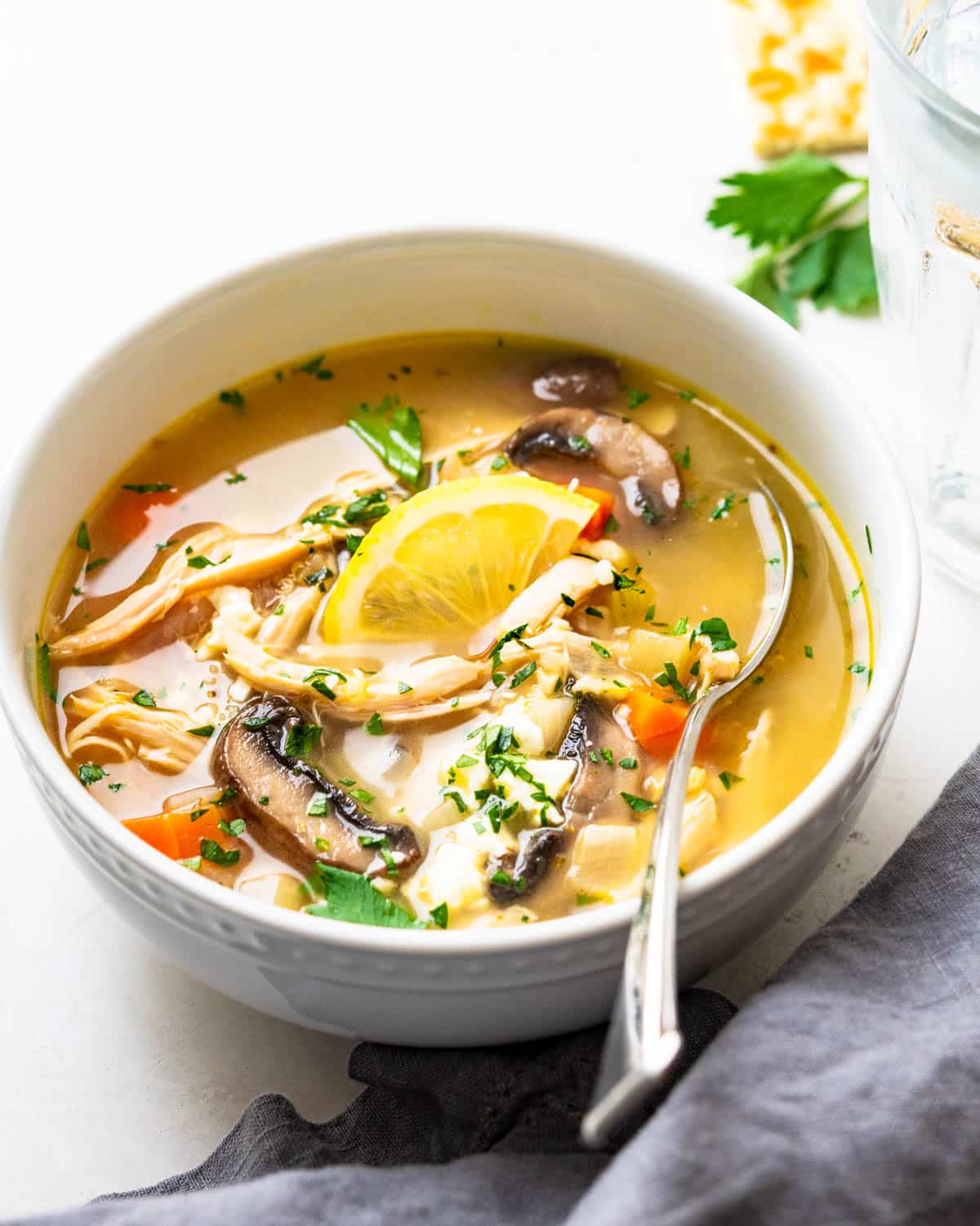 A bowl of lemon chicken soup with quinoa and slice of lemon.