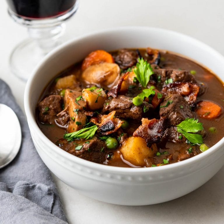 a bowl of beef stew with a glass of wine.
