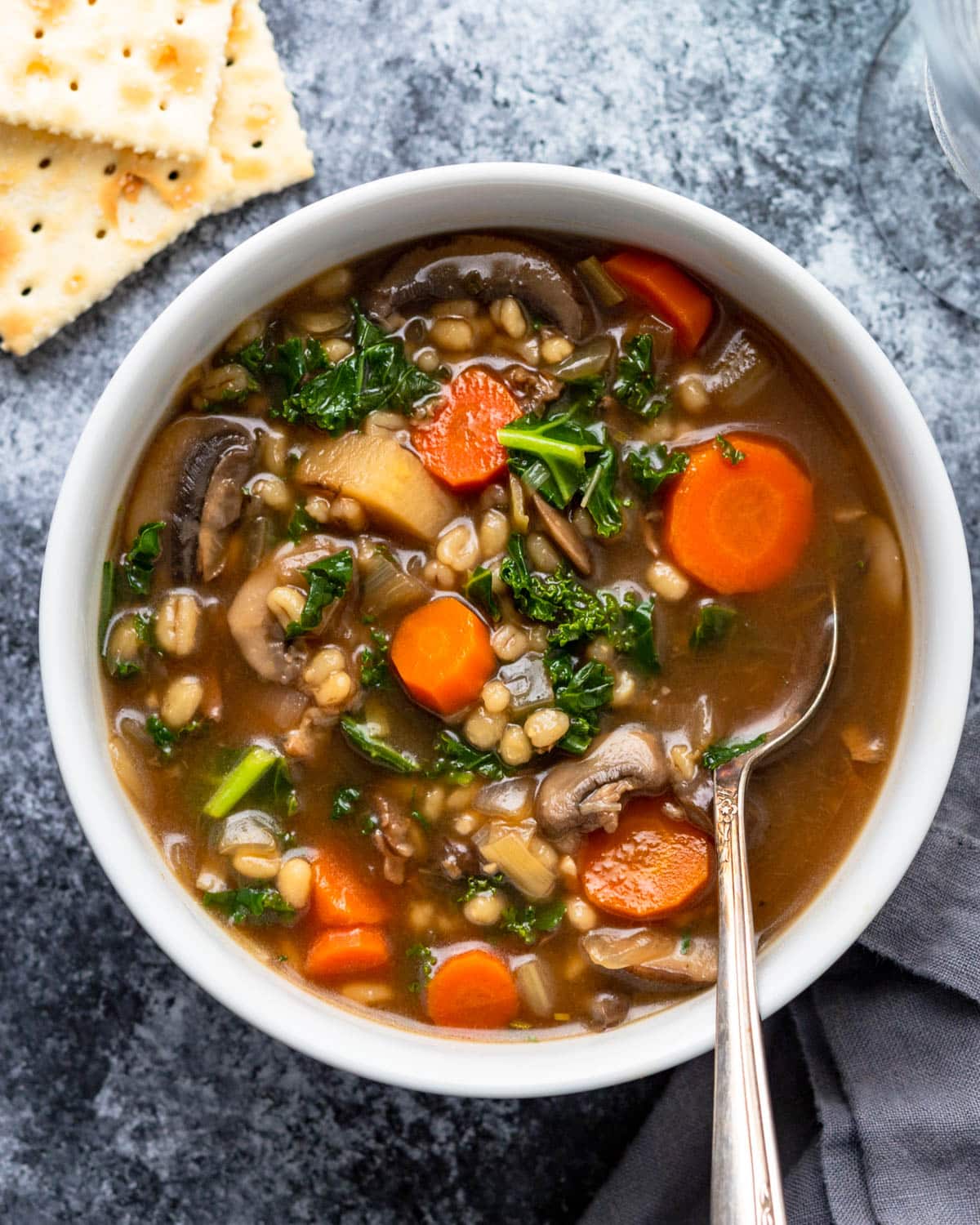 A bowl of mushroom barley soup with carrots and saltines on the side.
