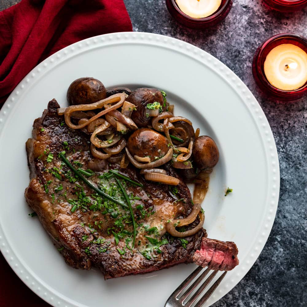 Pan seared ribeye with béarnaise butter, mushrooms and shallots on a plate.