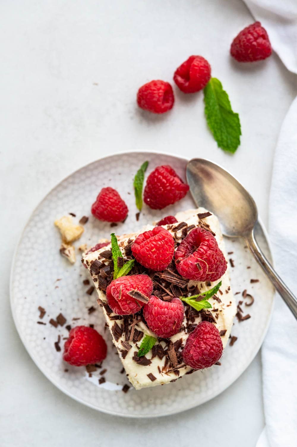 A serving of raspberry tiramisu on a plate with chocolate and mint.