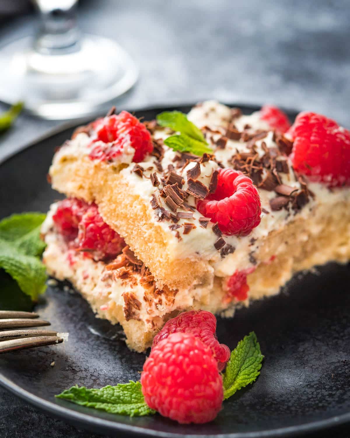 A dessert plate with raspberry tiramisu and extra berries and mint for garnish.