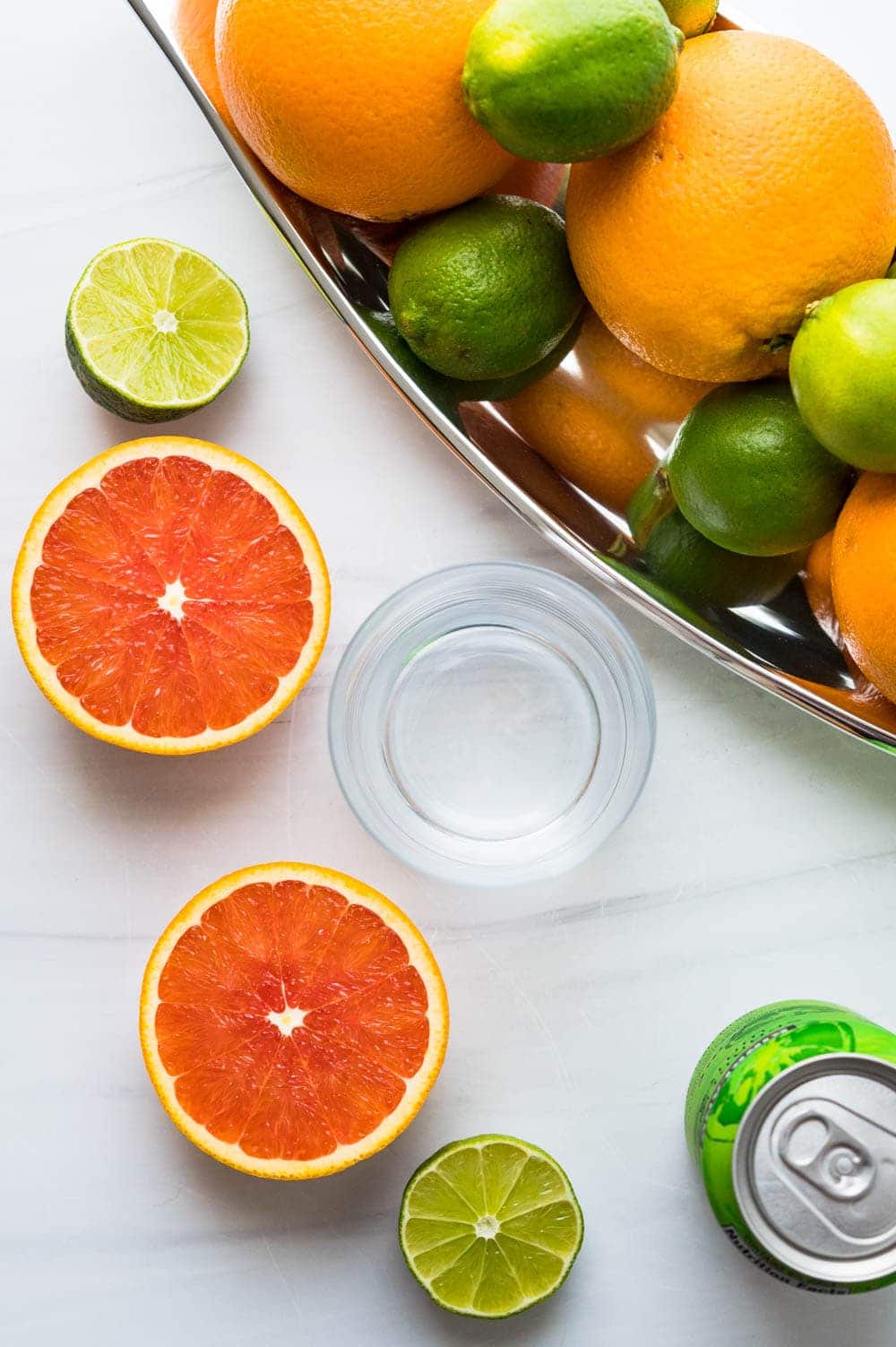 an overhead shot of sliced oranges and limes with sparkling water for a non alcoholic margarita.