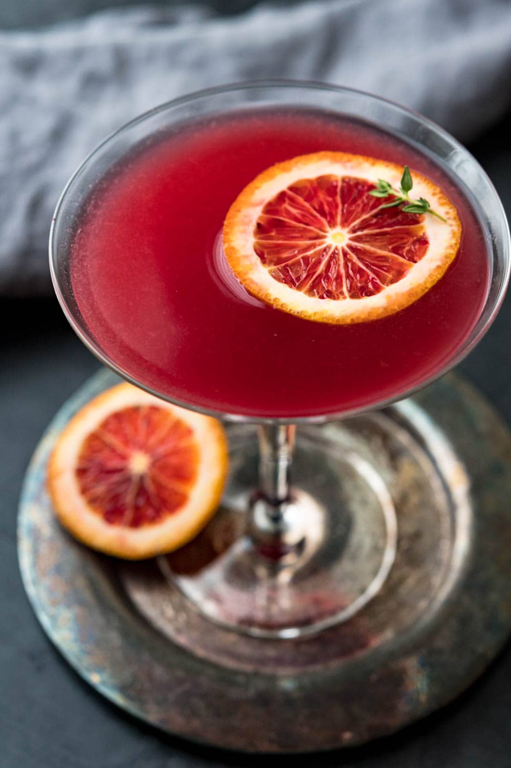 a moody image of the red cocktail with a slice of blood orange and sprig of thyme.