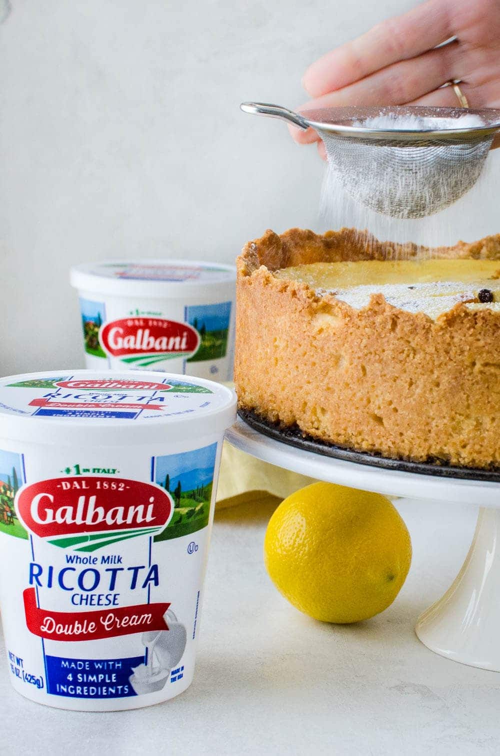 sprinkling sugar on the easter pie with a container of Galbani ricotta next to it.