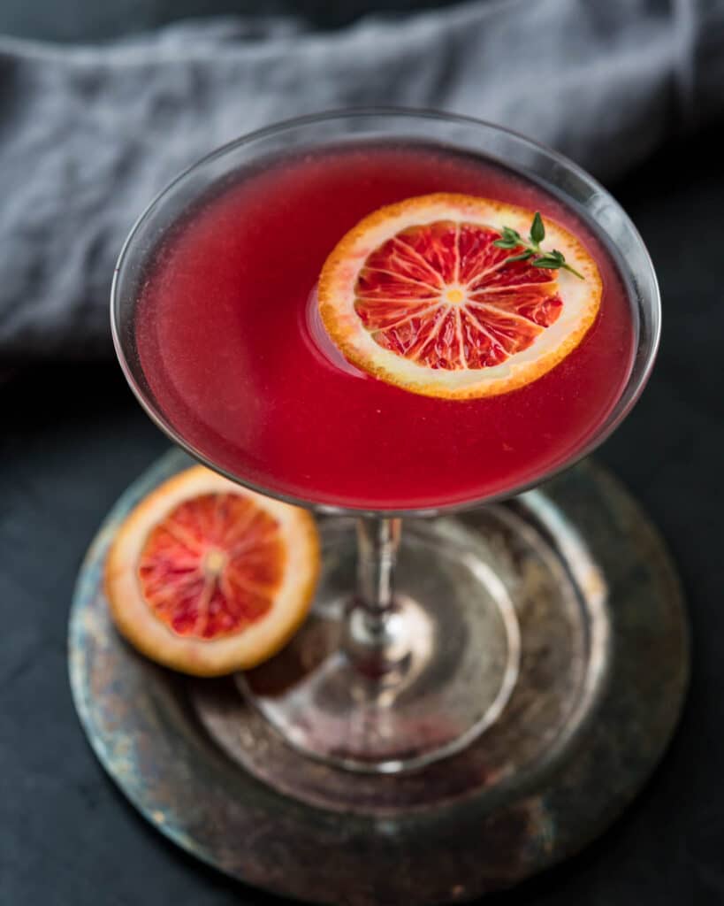 Serving a blood orange martini with a slice of fresh fruit floating on top.