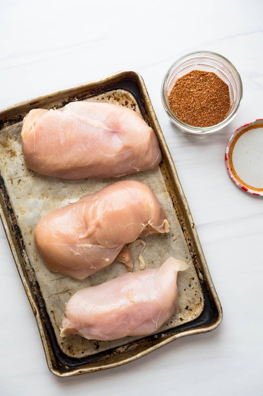 raw chicken breasts on a rimmed baking sheet.