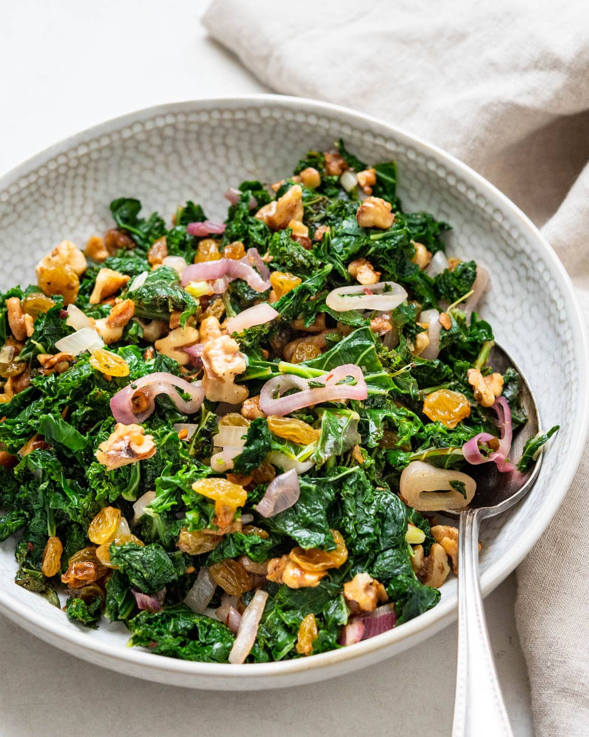A bowl of blanched kale with toasted walnuts and golden raisins.
