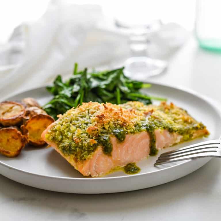 A serving of pesto salmon on a plate with spinach and potatoes.