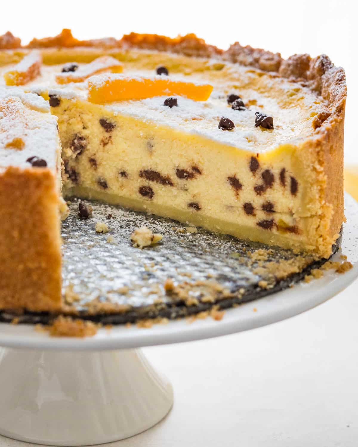 A citrus and chocolate chip Easter Ricotta Pie on a pedestal.