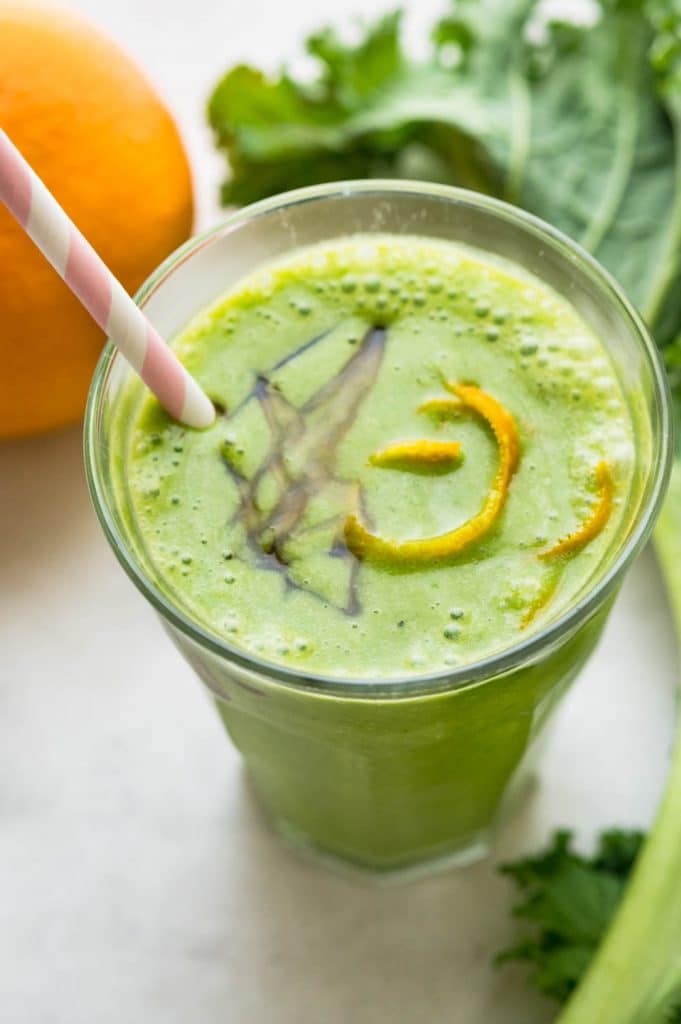 a photo of the green detox smoothie with a garnish of orange peel and a paper straw.