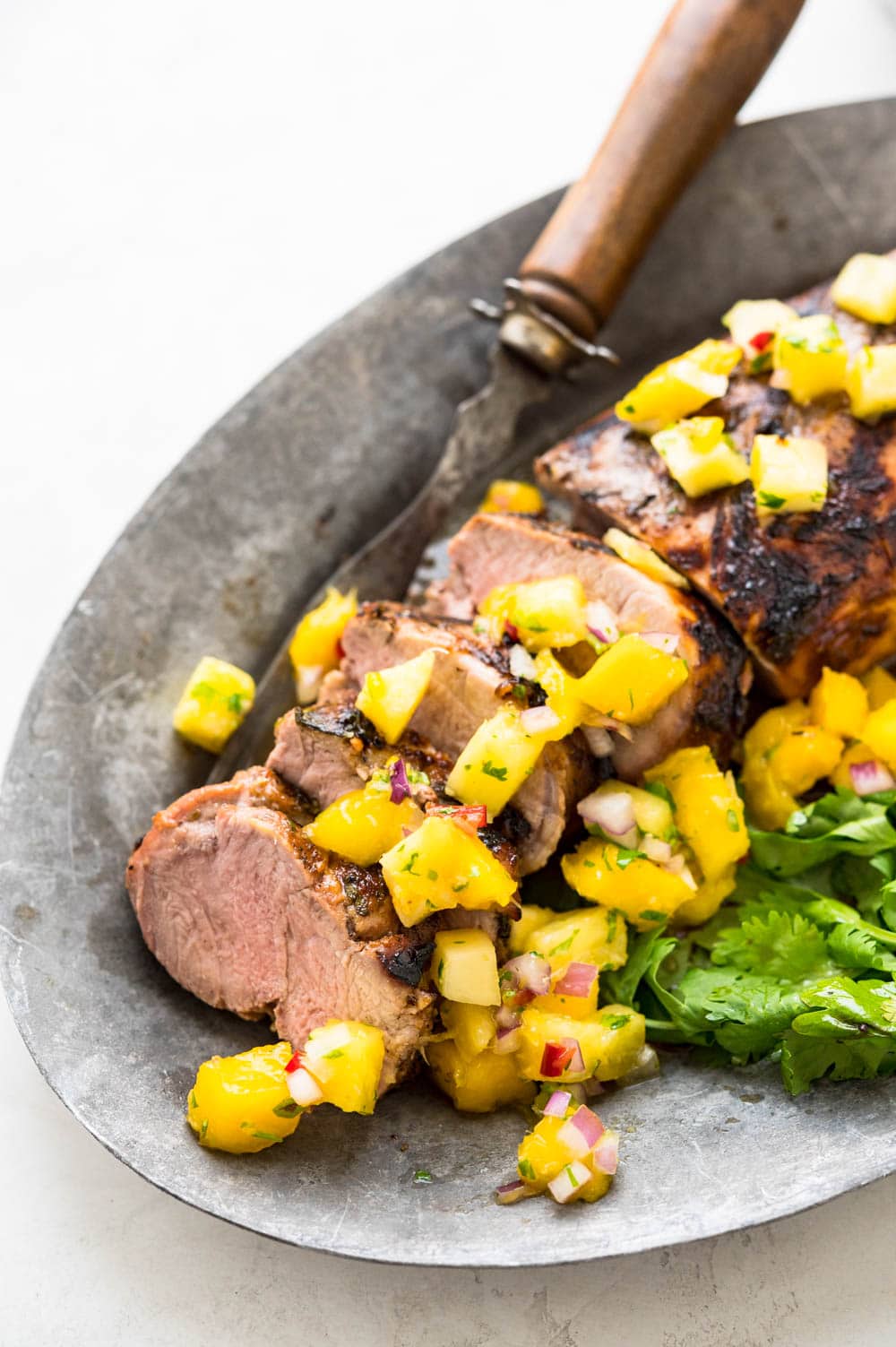 marinated grilled pork tenderloin on a platter with tropical salsa.