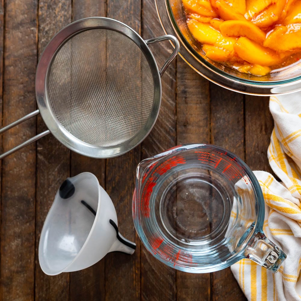 a funnel, strainer and glass measuring cup to strain the peach simple syrup.