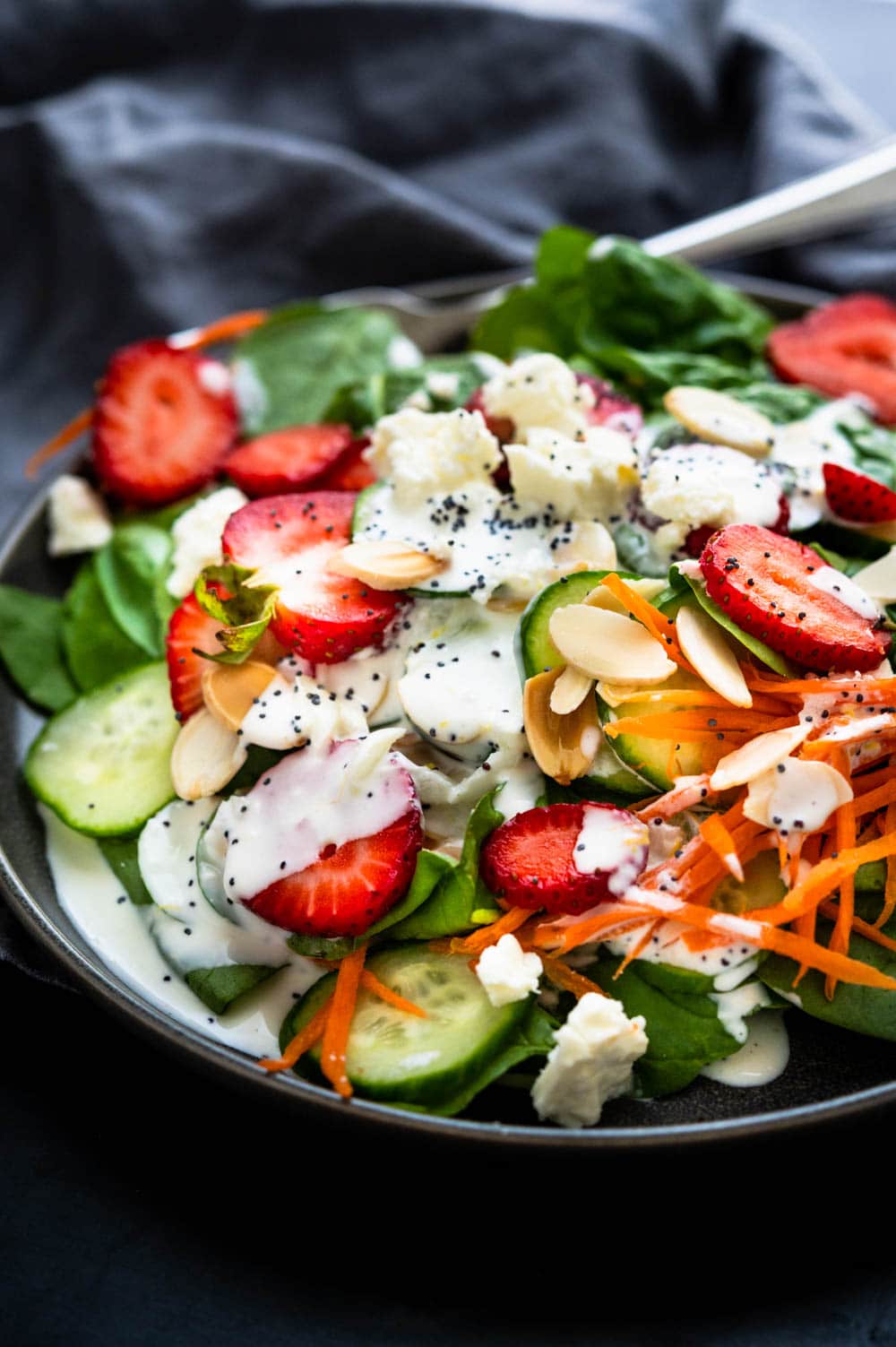 A dressed plate of strawberry and spinach salad with carrots, almonds and crumbled cheese.