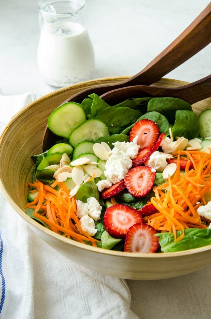 Assembling the spinach and strawberry salad in a salad bowl.