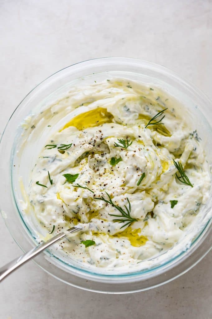 Cucumber yogurt sauce with herbs in a mixing bowl.