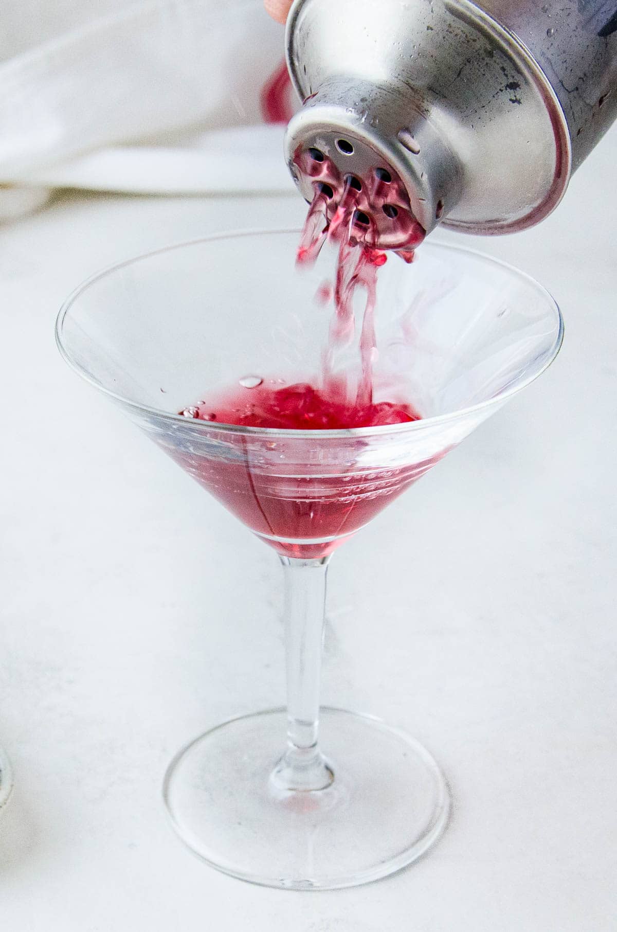 Straining the red drink into a martini glass.