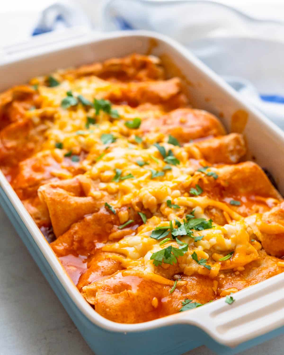 A casserole dish of beef enchiladas with cheese and cilantro.
