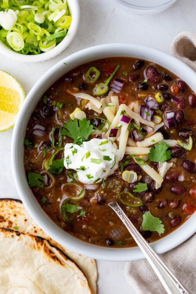 an overhead picture of the black bean chili with white cheddar, sour cream green and red onions and cilantro garnishes. 