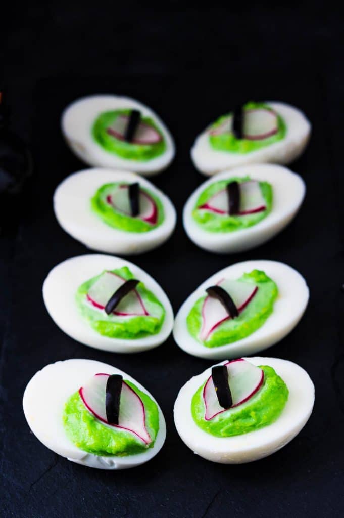 a black platter filled with Halloween deviled eggs that look like spooky green eyeballs. 