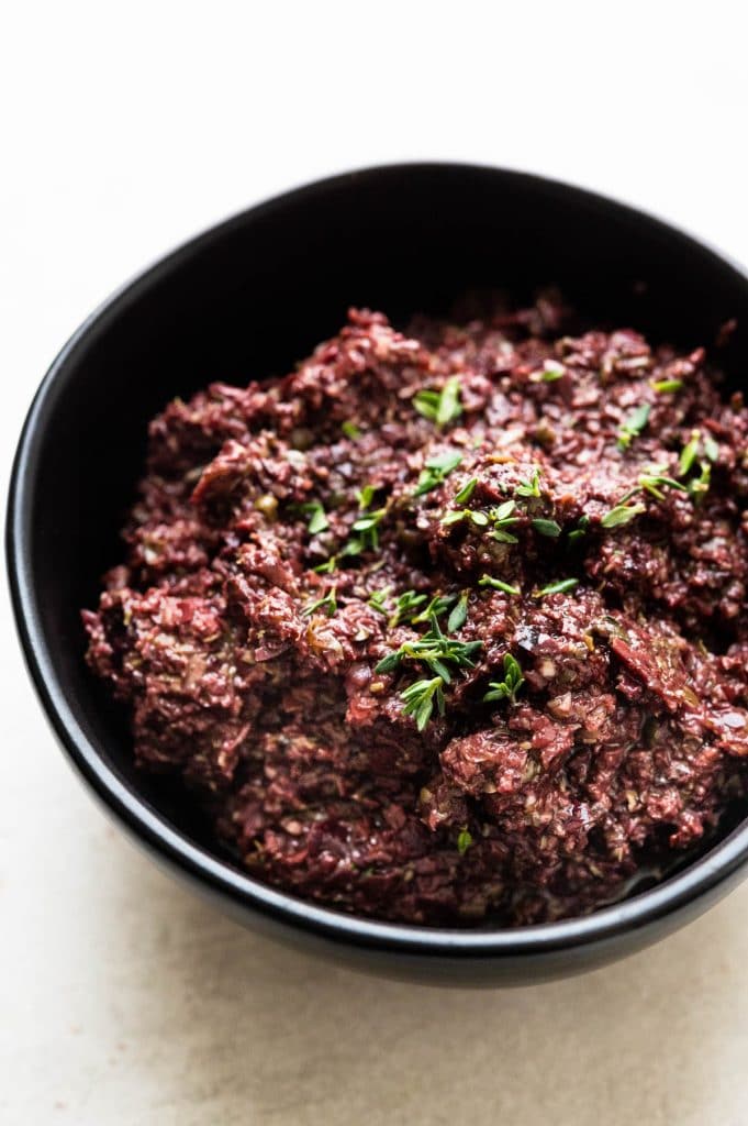 a bowl of kalamata tapenade with fresh thyme sprinkled over it.