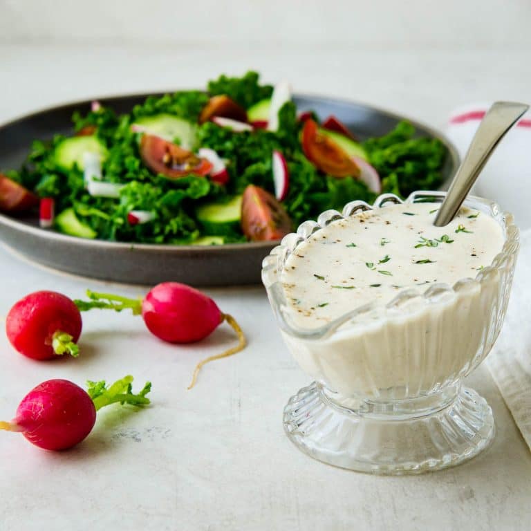 creamy garlic dressing in a glass carafe with a green salad.