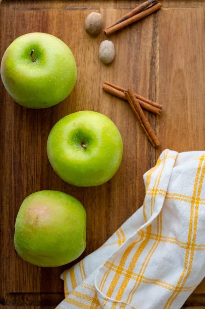 Granny Smith apples, cinnamon and nutmeg on a cutting board.