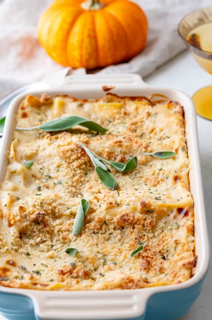 a sage embellished butternut squash lasagna, hot from the oven with a pumpkin in the background.