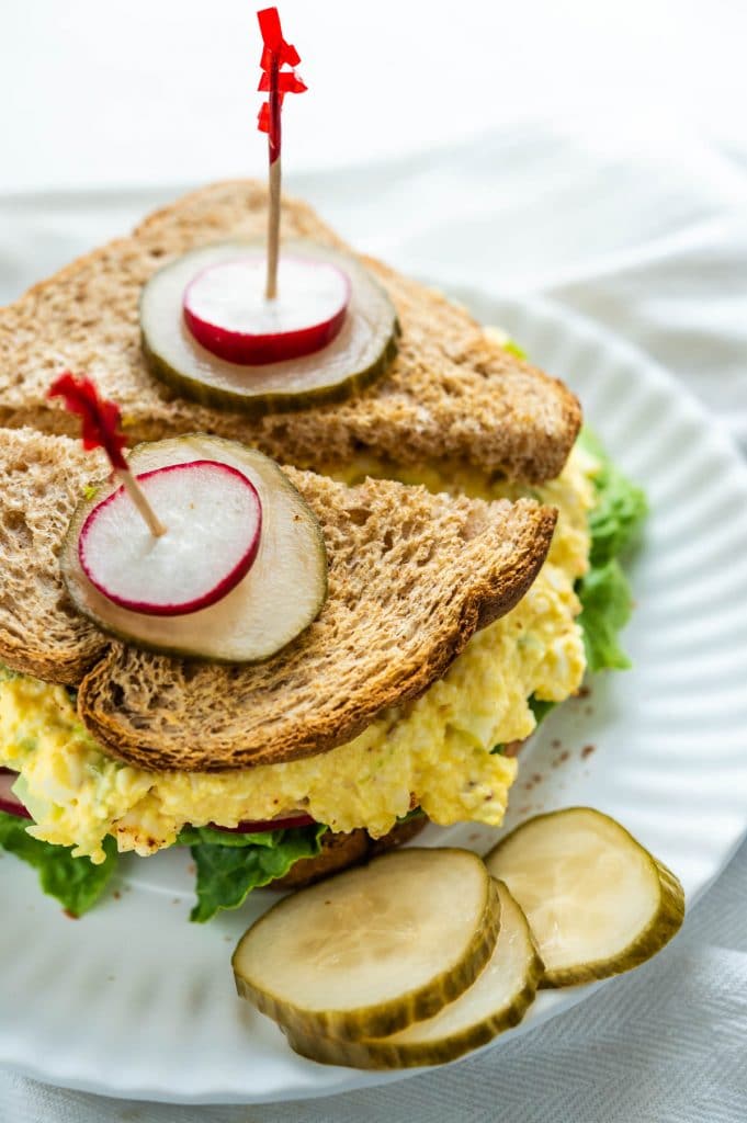 spearing the egg salad sandwich halves with pickles and toothpicks.
