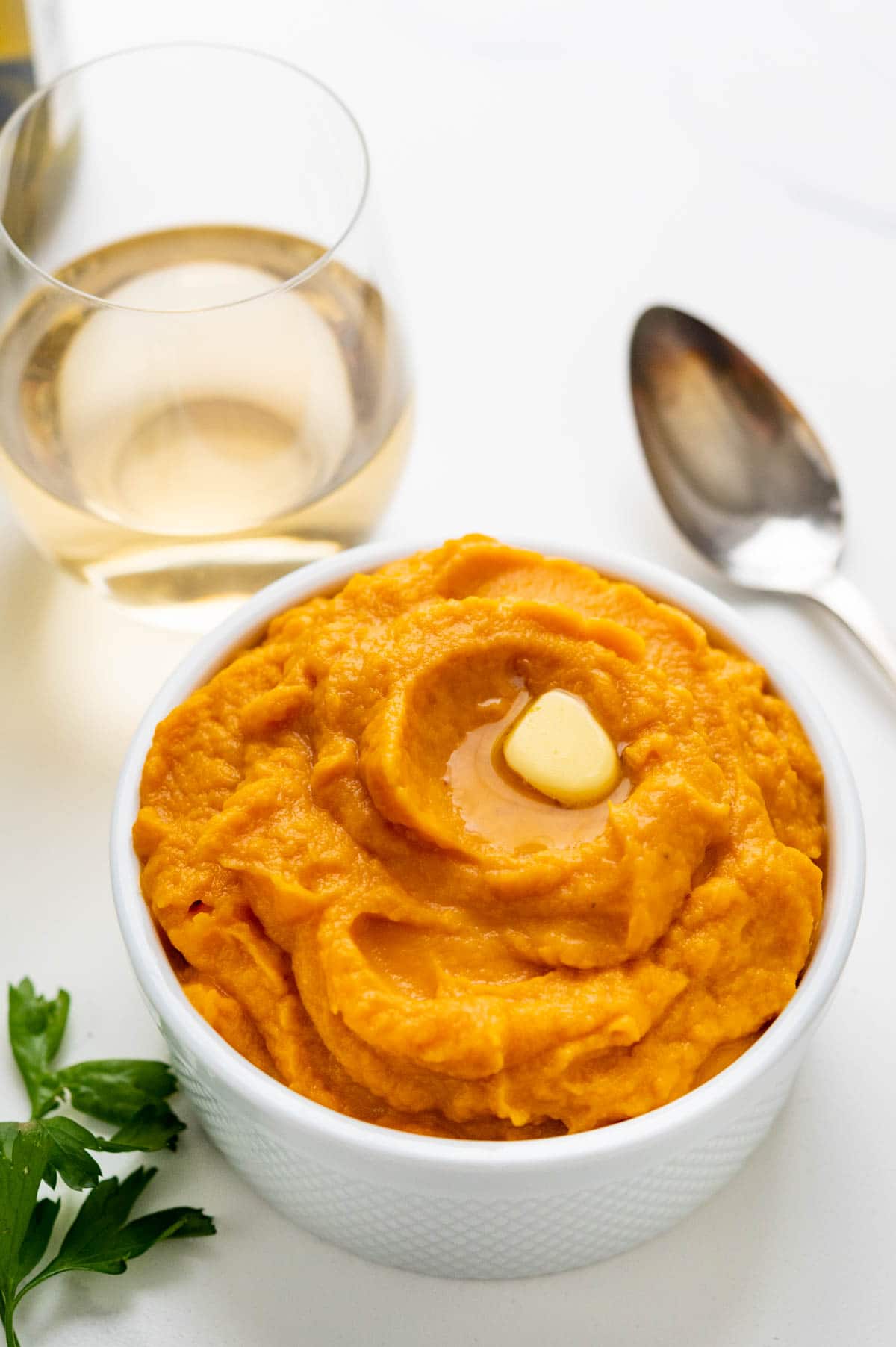 mashed sweet potatoes in a serving bowl with a pat of butter and a spoon.