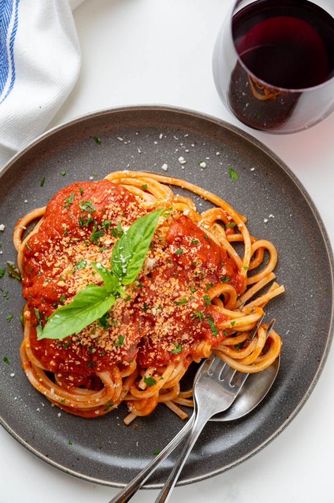 a plate of pasta pomodoro with grated cheese and a glass of red wine.