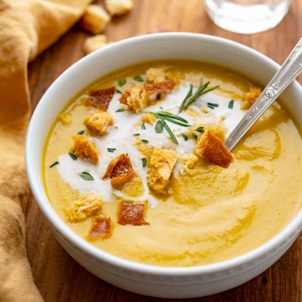 a bowl of roasted vegetable soup with croutons & cream.