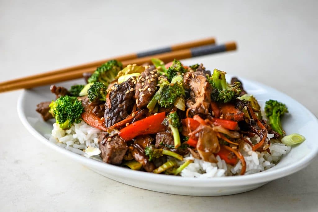 a serving of beef and broccoli over steamed rice with chopsticks.