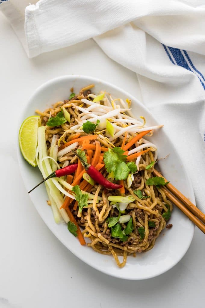 beef lo mein made with ground beef. Garnished with carrots, cucumber, green onions cilantro and lime.