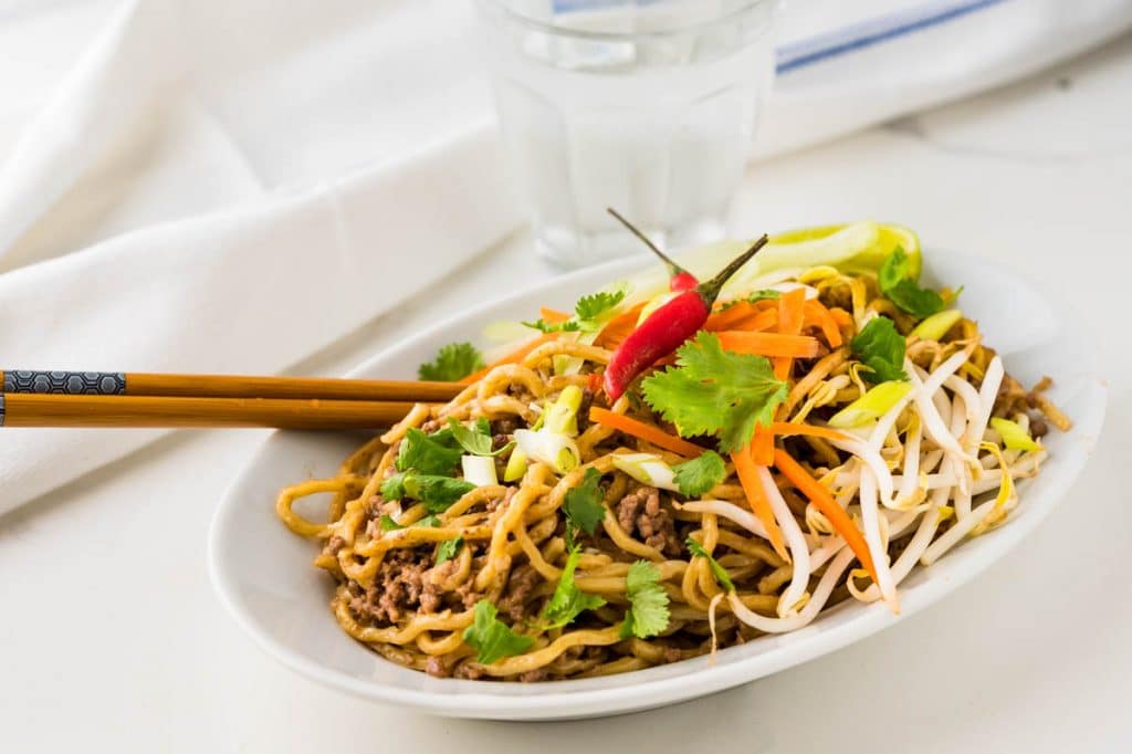 A serving of Ground beef lo mein with bean sprouts and thai chile peppers.