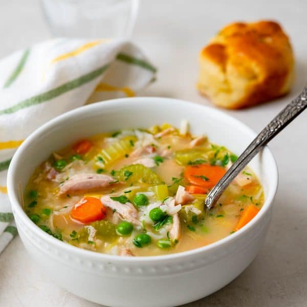 a serving of turkey rice soup with a roll on the side.