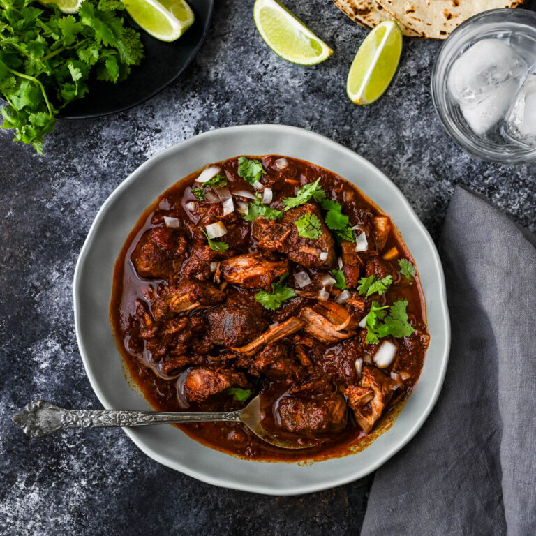 beef Birria in a bowl with limes, cilantro and white onion.