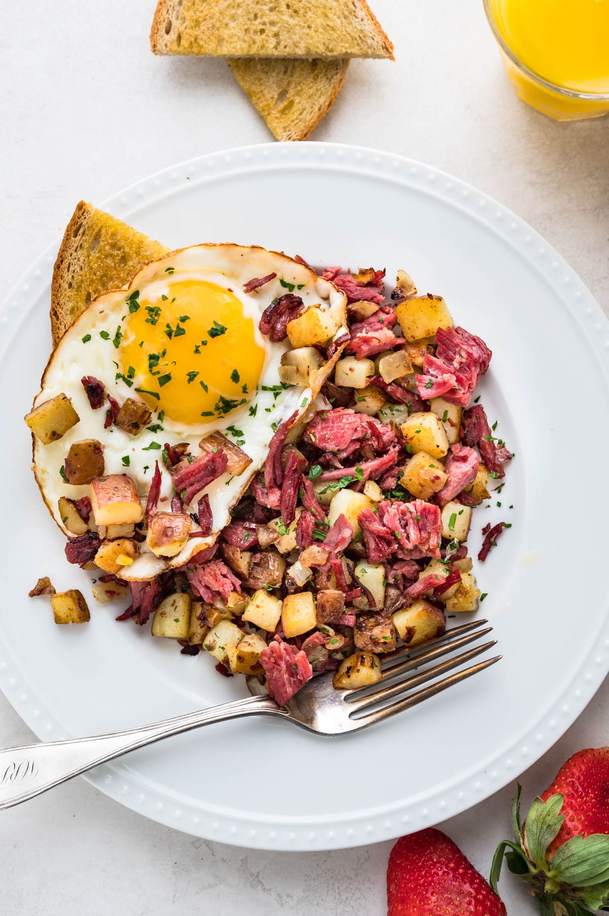 A serving of corned beef hash with fried eggs, toast and juice for breakfast.
